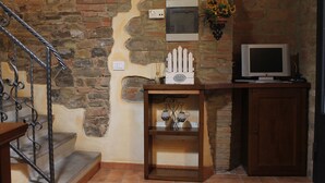 A staircase with metal railings, a stone wall, a wooden cabinet, a television, and a small shelf with decorative items.