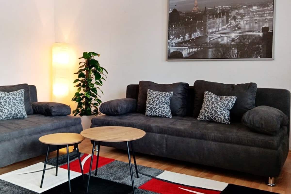 A modern living room with two sofas, a coffee table, a potted plant, and a cityscape painting on the wall.