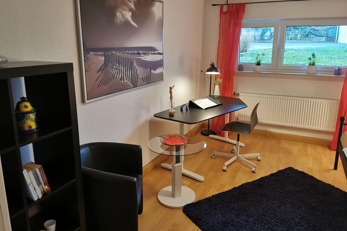 A modern room with a desk, chair, bookshelf, and a window with a view of greenery.