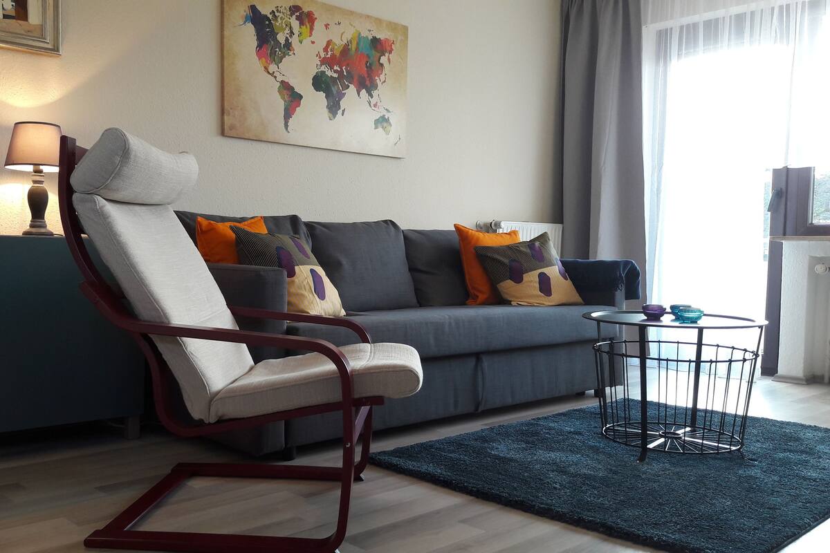 A modern living room with a grey sofa, a red rocking chair, a small round table, and a world map on the wall.
