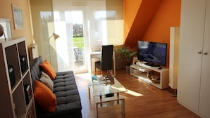A modern living room with a sofa, a glass coffee table, a TV, and a dining area with a chair and table. - Apartmenthaus Abendsonne (Koblenz)