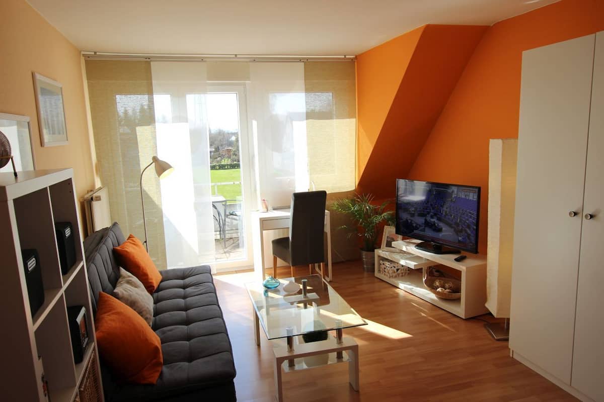 A modern living room with a sofa, a glass coffee table, a TV, and a dining area with a chair and table.