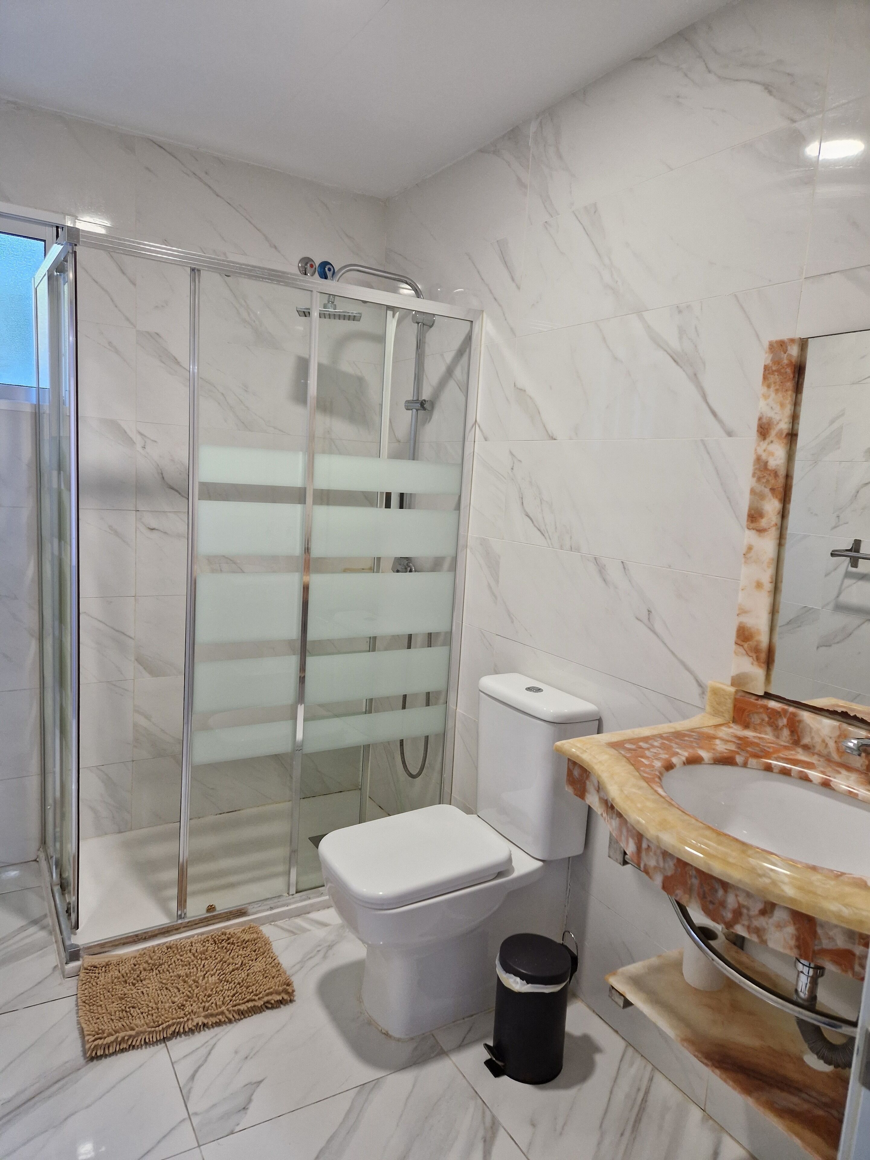 Ein Badezimmer mit einer Duschkabine, einer Toilette und einem Waschbecken mit Marmorplatte.