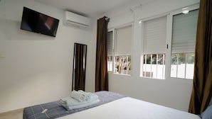 A bedroom with a bed, a flat-screen TV mounted on the wall, and a window with curtains. - Rancho Grande (Marbella)