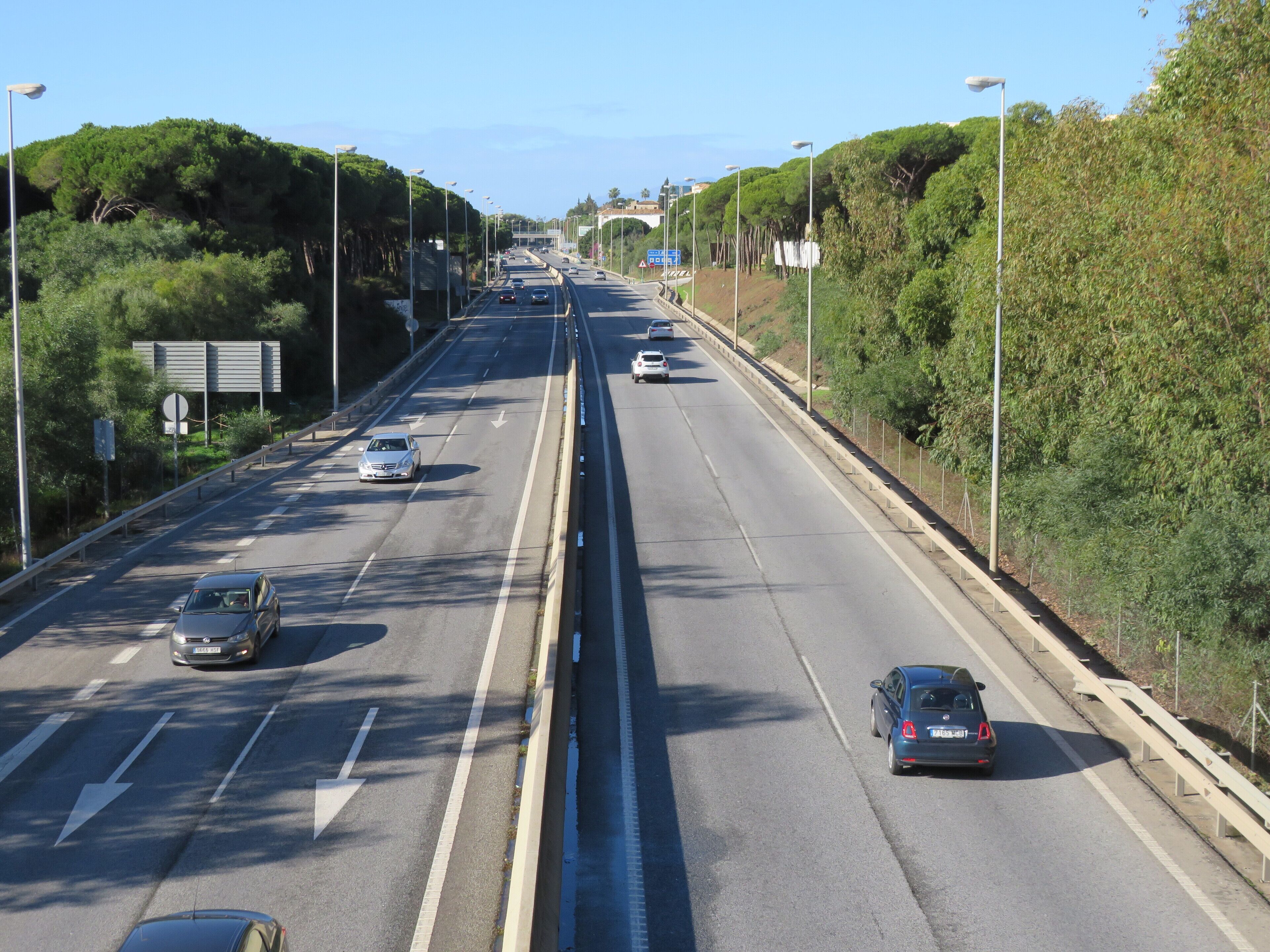 A multi-lane highway with vehicles, surrounded by greenery and streetlights.