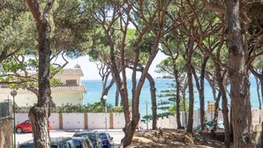 A coastal street lined with parked cars and trees, leading to a building with a tiled roof. - Rancho Grande (Marbella)