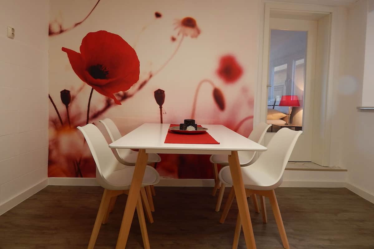 Ein Essbereich mit einem weißen Tisch und Stühlen, einer roten Tischmatte und einer Wandmalerei von roten Blumen.