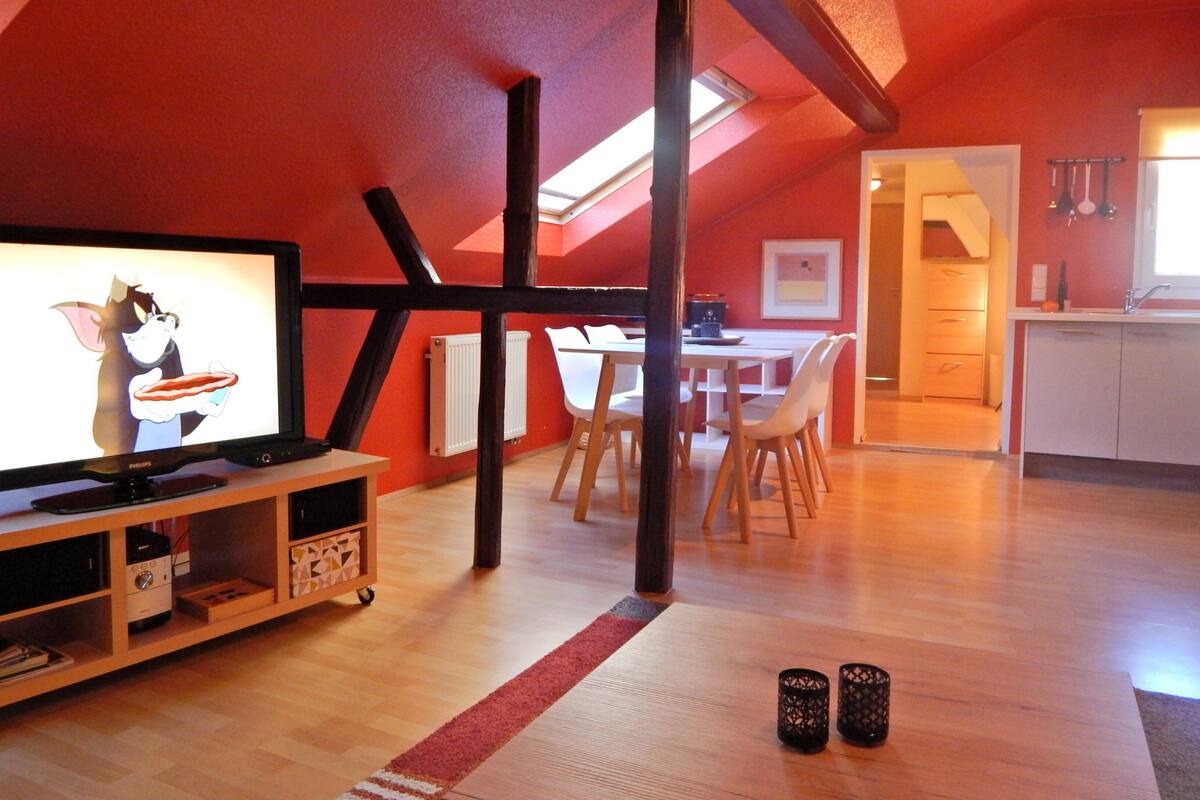 Ein modernes Loft mit roter Decke, Holzbalken, einer Essecke mit weißen Stühlen und einer Küche mit weißen Schränken.
