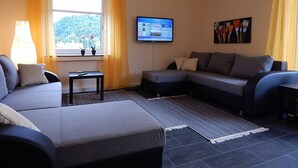 A modern living room with a grey sofa, a small table, and a TV mounted on the wall. - Ferienwohnung Koblenz City (Koblenz)