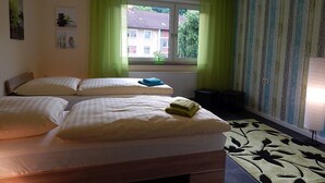 A bedroom with two beds, a window with curtains, a radiator, a small plant, and a patterned rug. - Ferienwohnung Koblenz City (Koblenz)