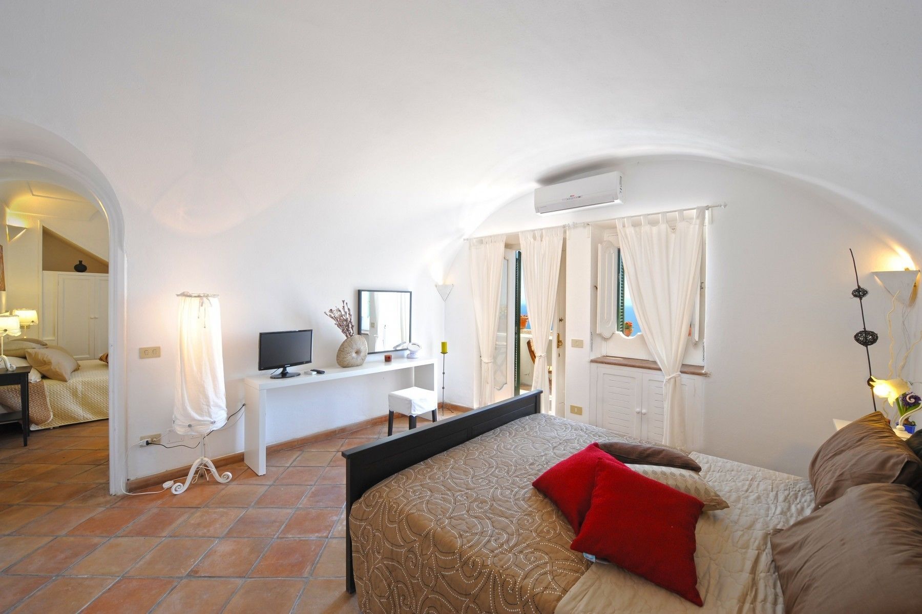 Une chambre à coucher avec un lit, un bureau, une télévision et une fenêtre avec des rideaux.