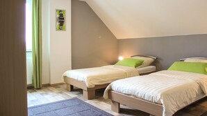 Een slaapkamer met twee eenpersoonsbedden, een houten vloer, een groen gordijn en een afbeelding in een lijst aan de muur.