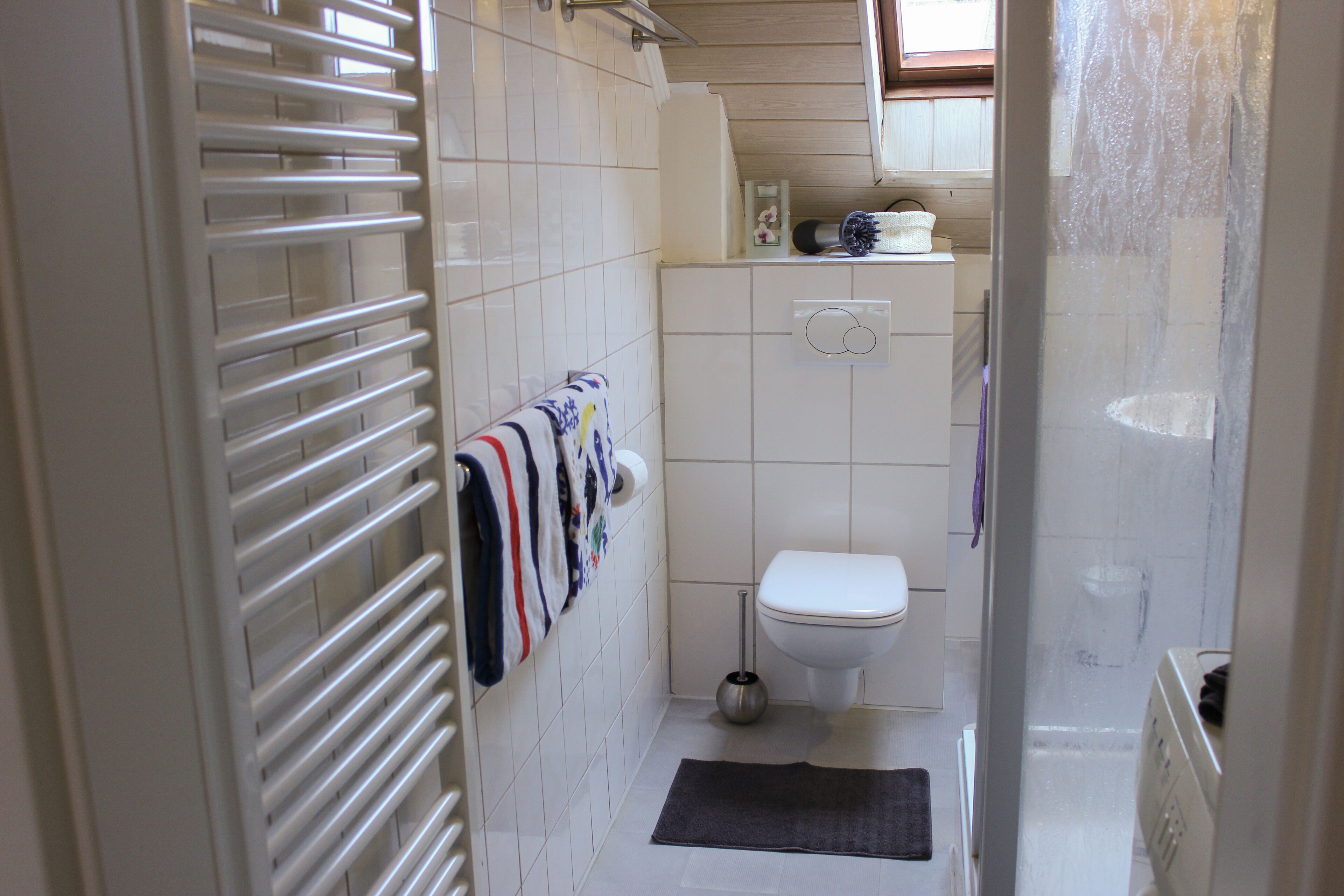 A small bathroom with a toilet, a towel rack with towels, a shower, and a toilet paper holder.