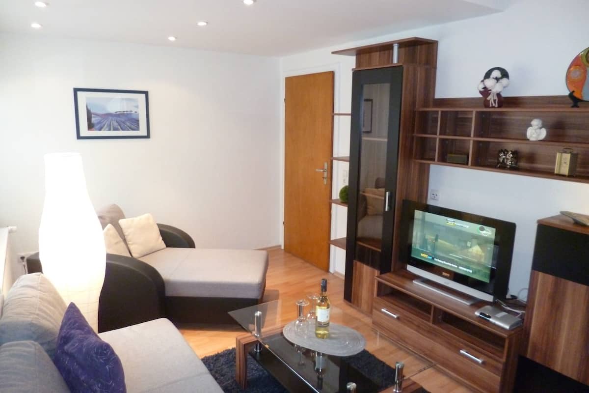 Ein modernes Wohnzimmer mit einer Couch, einem Glastisch, einem Fernseher und einem Holzschrank.