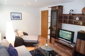 A modern living room with a sofa, a glass coffee table, a television, and a wooden cabinet.