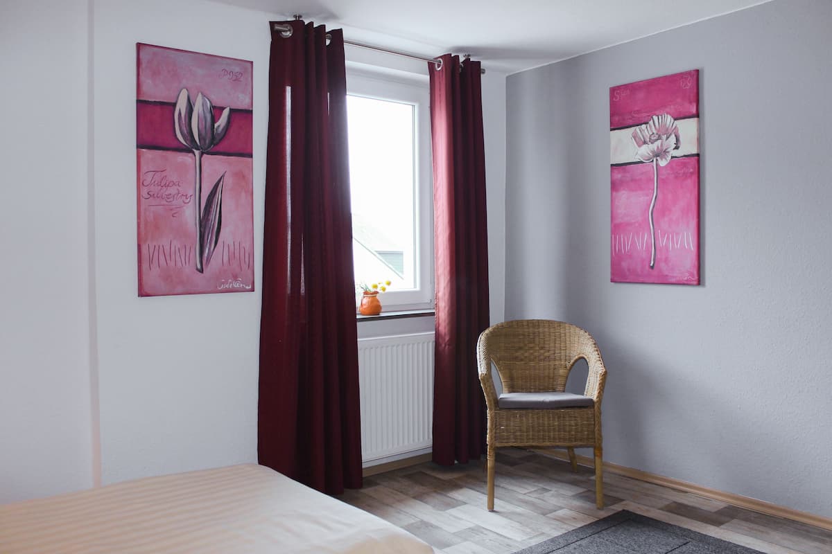 Ein Schlafzimmer mit einem Bett, einem Korbstuhl und zwei Bildern an der Wand.