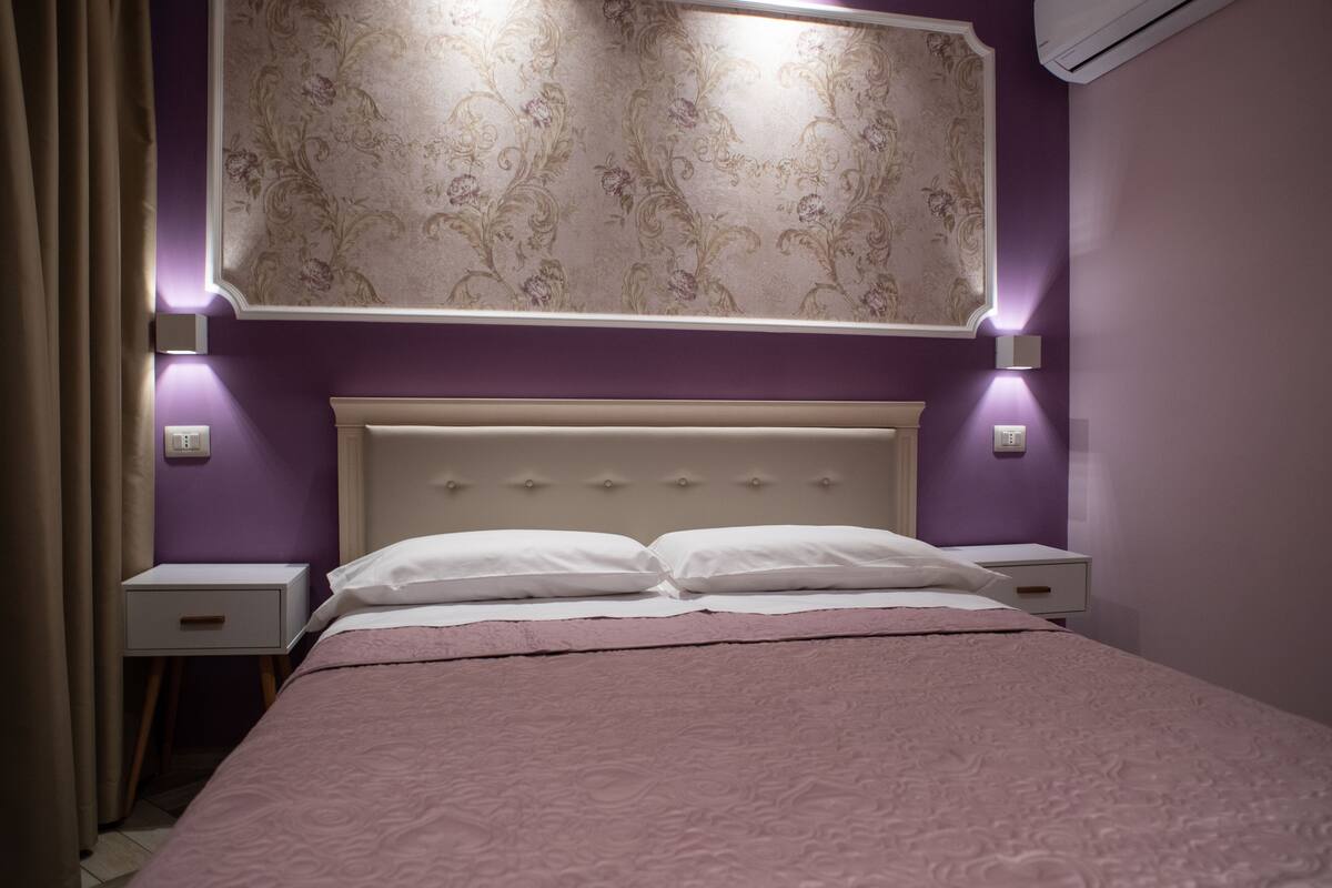 Un dormitorio con cama, mesitas de noche y cabecera con iluminación empotrada.