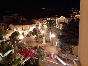 Vue nocturne d’une place historique, avec ses bâtiments, ses palmiers et ses lampadaires.