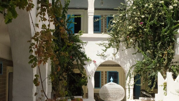 Une cour avec des murs blancs, des portes bleues et une lanterne décorative.