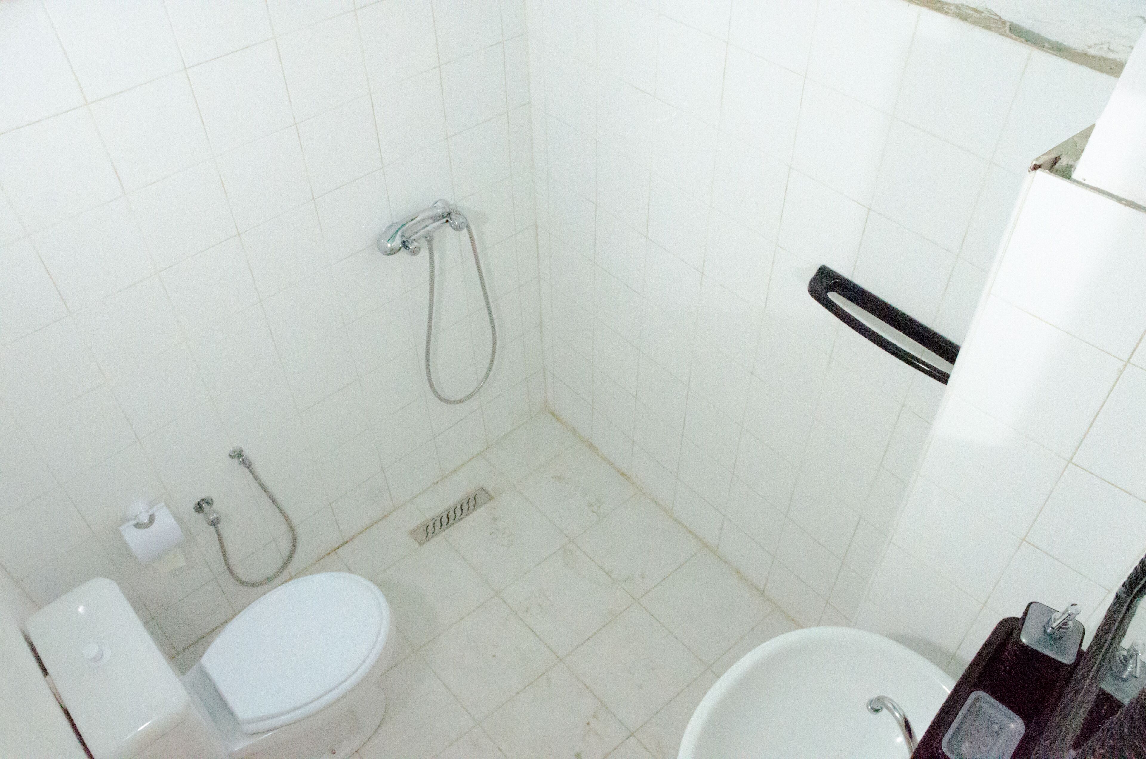 Une petite salle de bain propre, avec des carreaux blancs, des toilettes, une douche et un lavabo.
