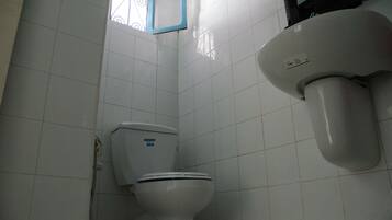 Une salle de bain avec des murs recouverts de carreaux blancs, des toilettes, une douche et une fenêtre à cadre bleu.