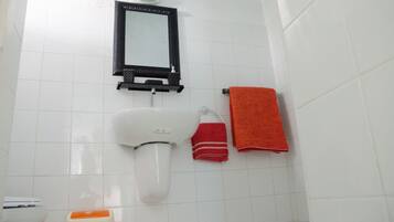Un baño con inodoro blanco, espejo con marco negro y dos toallas, una roja y otra naranja.