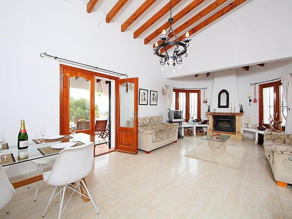 A spacious living room with a glass dining table, a sofa, a fireplace, and a chandelier.