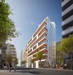 A modern multi-story building with balconies, surrounded by trees and other buildings.