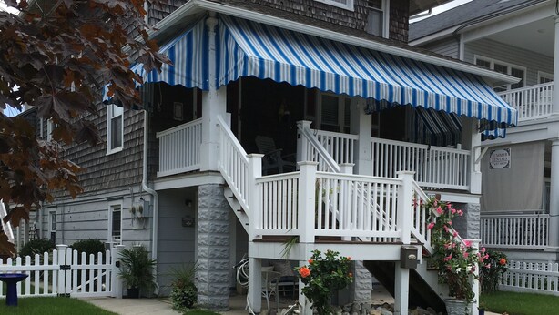 A two-story house with a covered front porch, a white picket fence, and a stone foundation. - OCNJ Gold Coast beach home, Pet friendly, 9 houses from the beach and boards!  (Ocean City)