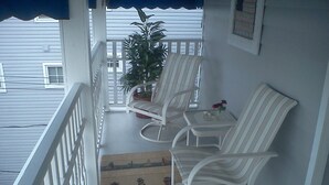 A balcony with white wicker chairs and a small table, a potted plant, and a rug with a nautical design. - OCNJ Gold Coast beach home, Pet friendly, 9 houses from the beach and boards!  (Ocean City)