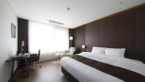 A modern hotel room with a large bed, a desk with a laptop, a chair, and a small round table.