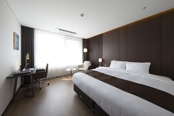Una habitación de hotel moderna con una cama grande, un escritorio con una computadora portátil, una silla y una pequeña mesa redonda.