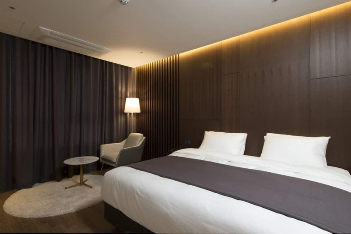 A modern hotel room with a large bed, a small round table, a chair, and a lamp.