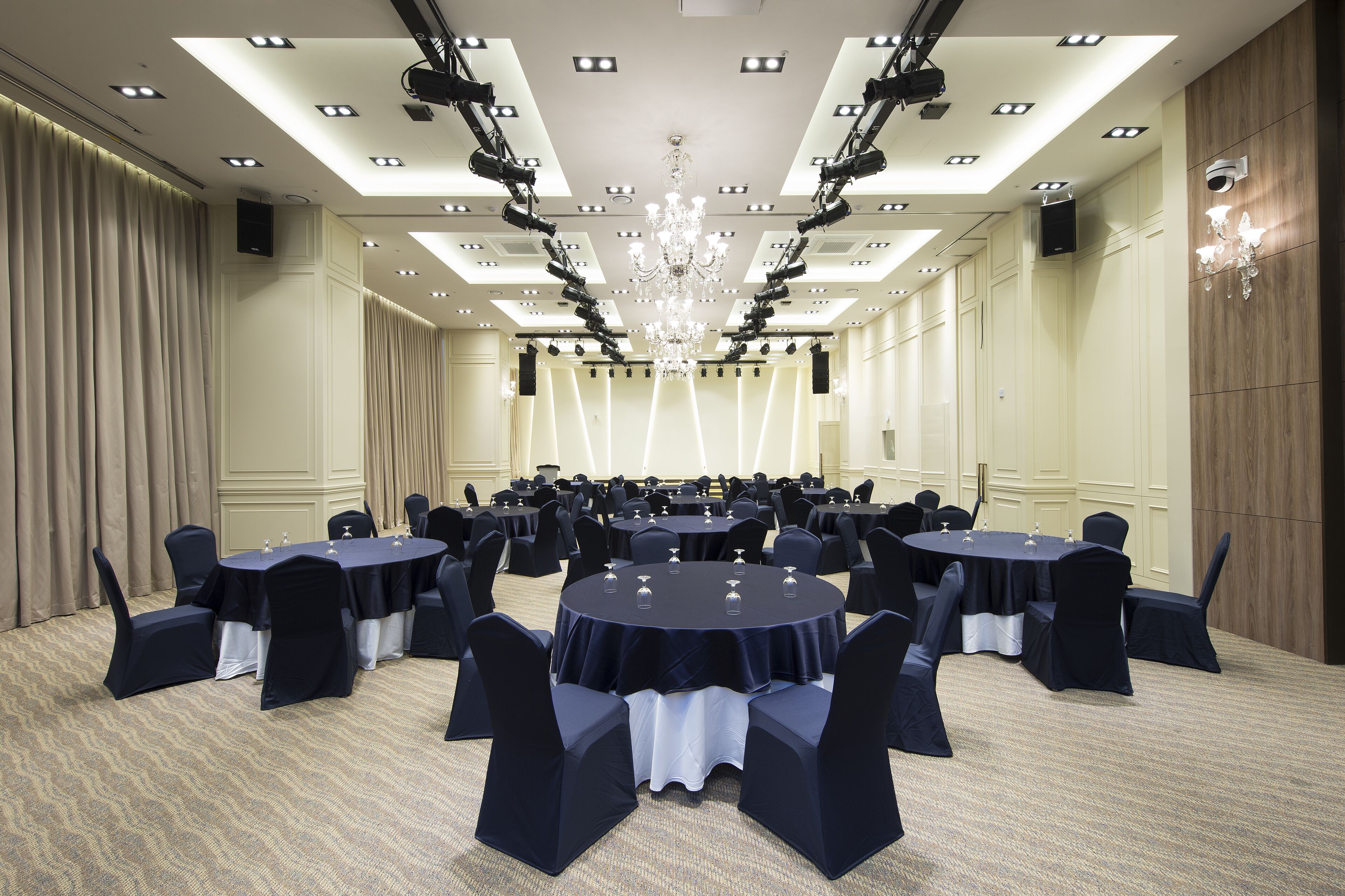 Un amplio salón de conferencias con varias mesas redondas, cada una rodeada de sillas, y un candelabro colgando del techo.
