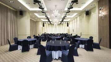 Un amplio salón de conferencias con varias mesas redondas, cada una rodeada de sillas, y un candelabro colgando del techo.