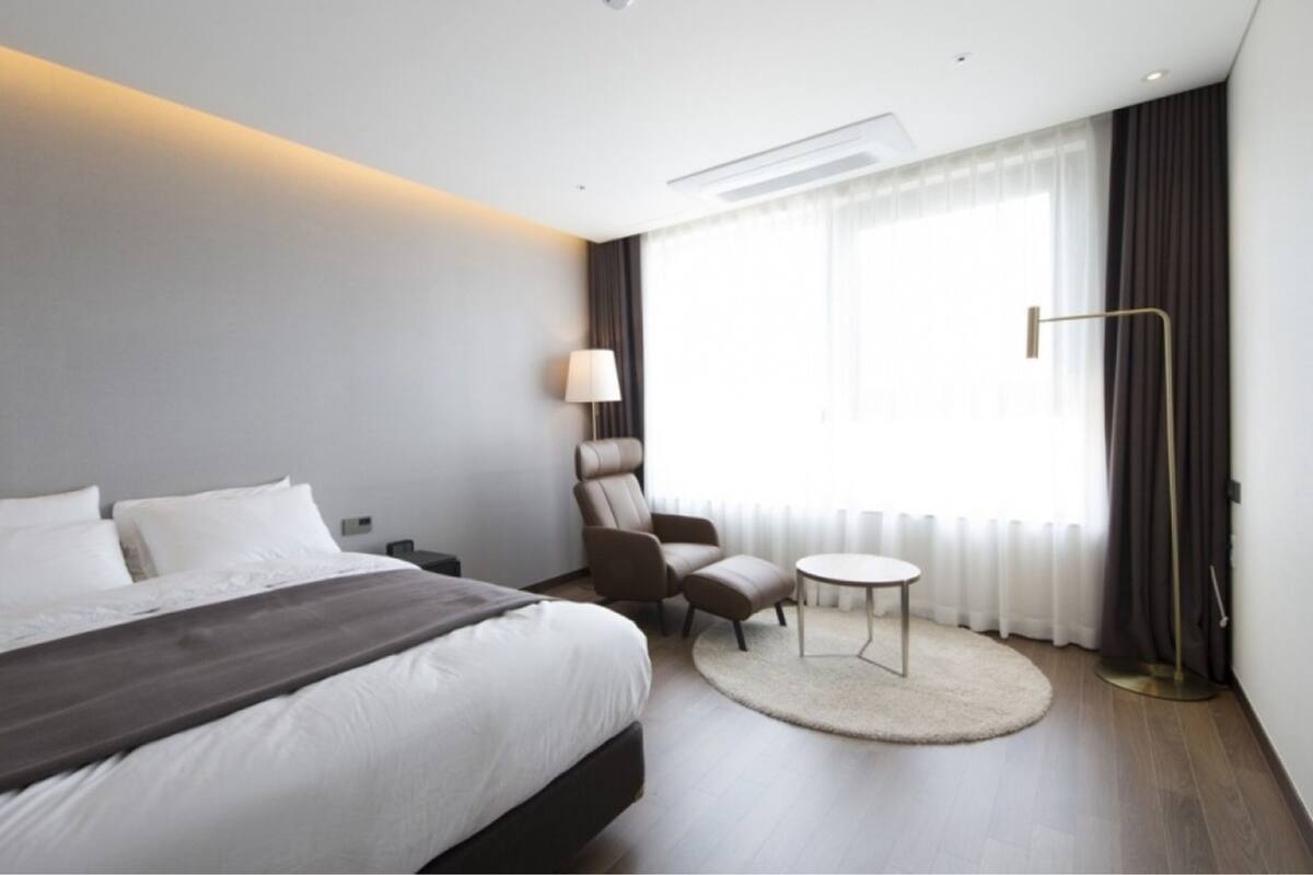 A modern hotel room with a large bed, a small round table, a chair, and a lamp.