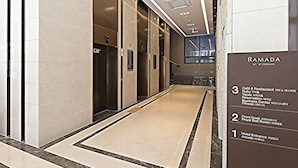 A modern hotel lobby with a marble floor, elevators, and a sign indicating the location of the hotel entrance, café, restaurant, and fitness center.