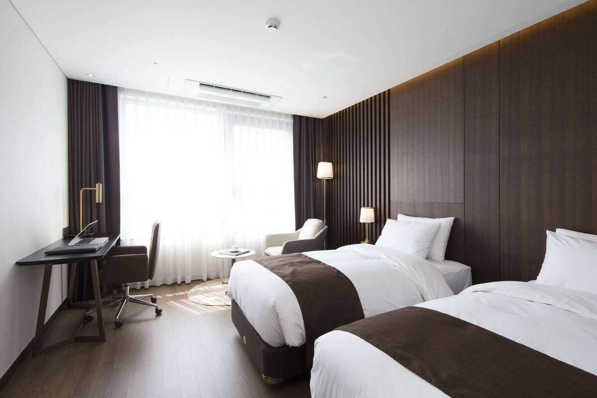 A hotel room with two beds, a desk, a chair, and a small table.