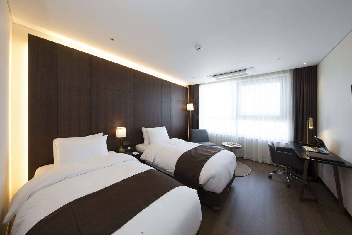 A hotel room with two beds, a desk, and a chair.