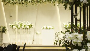 A formal event space with a long aisle, chairs on one side, and floral decorations.