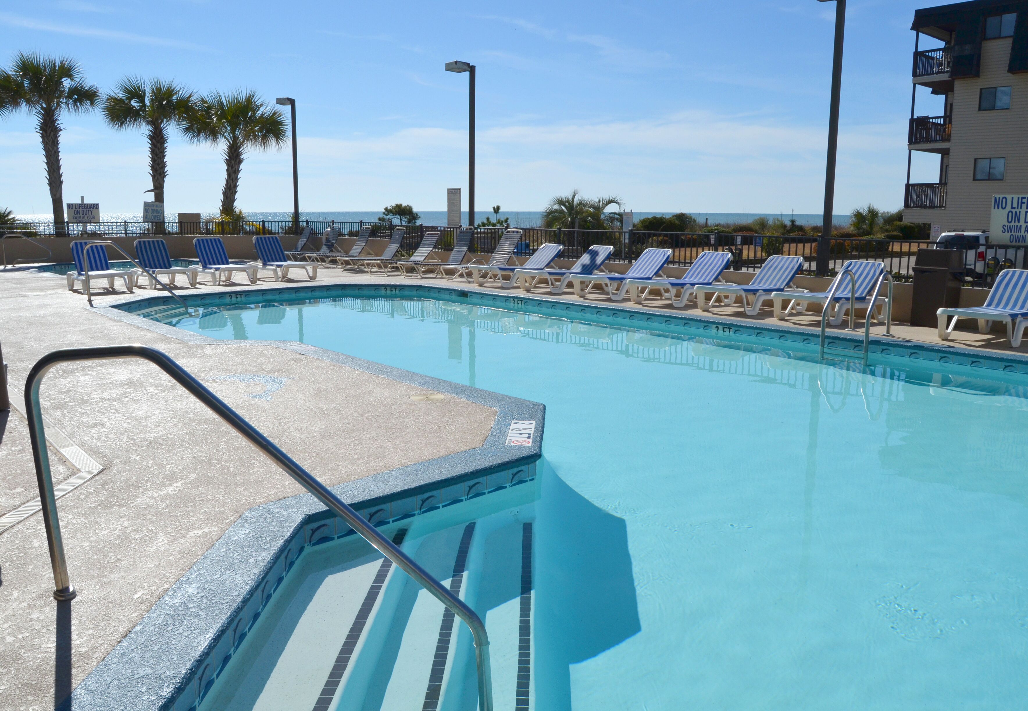 A pool area with lounge chairs and a view of the ocean.