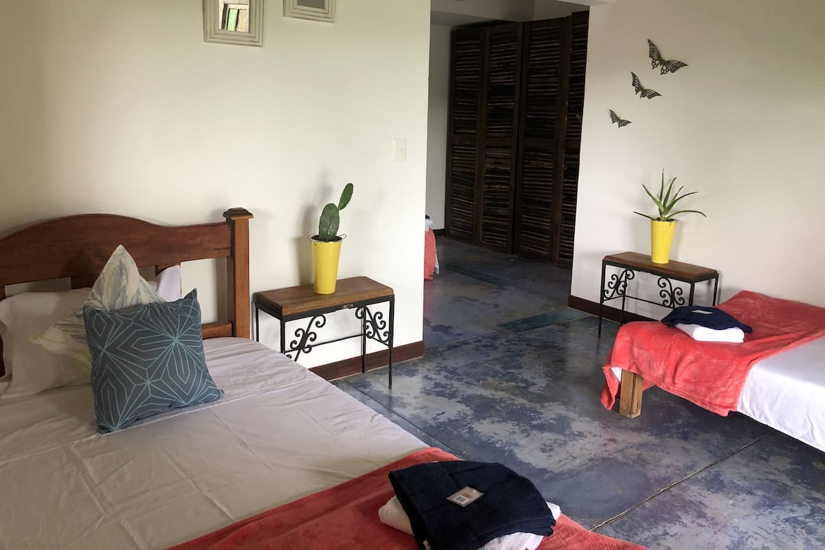 Een hotelkamer met twee bedden, een houten hoofdeinde, een klein tafeltje met een bloempot en een wand met vlinderdecoraties.