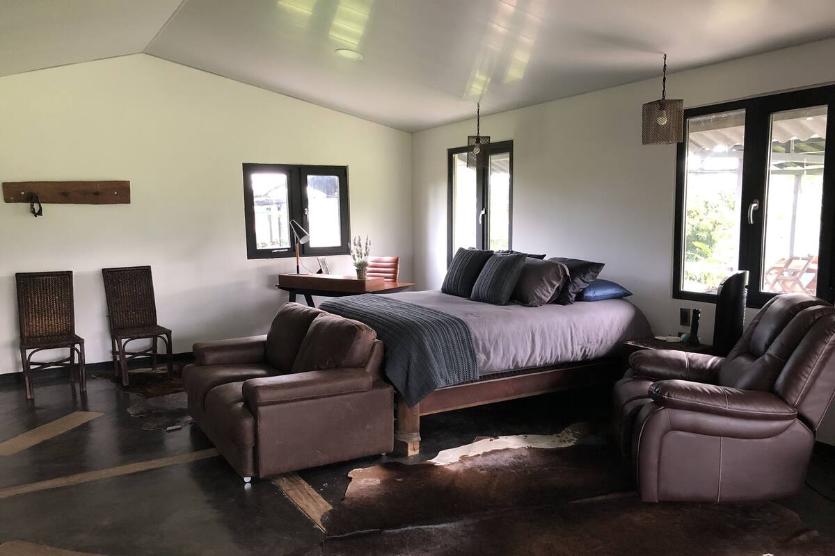 Een slaapkamer met een bed, twee lederen fauteuils, een bureau en een groot raam.