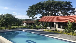A swimming pool with a tiled deck, a covered outdoor seating area, and a building with a red-tiled roof. - Finca Hotel Brasilia (La Tebaida)