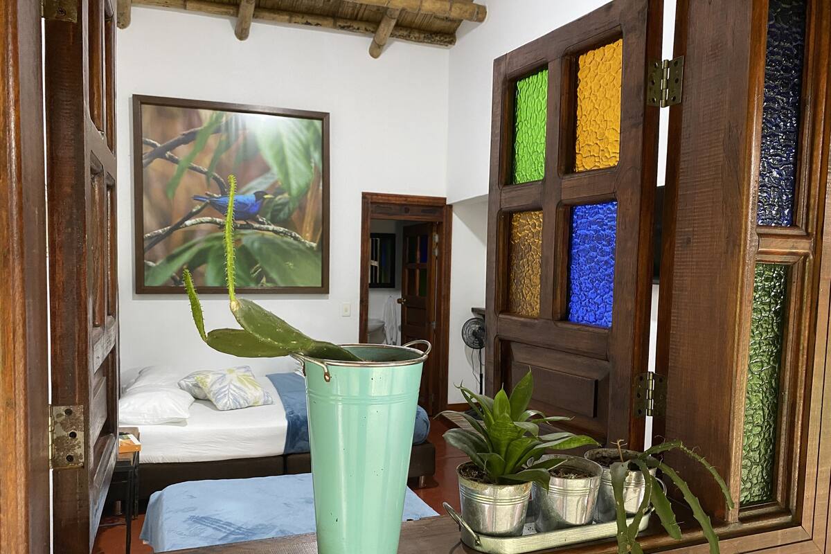 Een kamer met een bed, een raam met kleurrijk glas-in-lood en een bloempot op een houten plank.