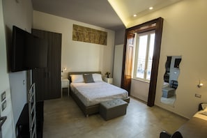 A modern bedroom with a large bed, a TV, and a mirror. - Bayard101 (Naples)
