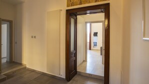 A hallway with a radiator, a wooden door, and a view into another room. - Bayard101 (Naples)