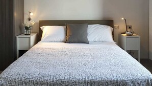 A modern bedroom with a large bed, two bedside tables, a nightstand, and a decorative wall piece. - Bayard101 (Naples)