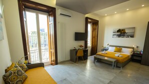 A hotel room with a bed, desk, and chair, a TV mounted on the wall, and a window with a view of buildings. - Bayard101 (Naples)