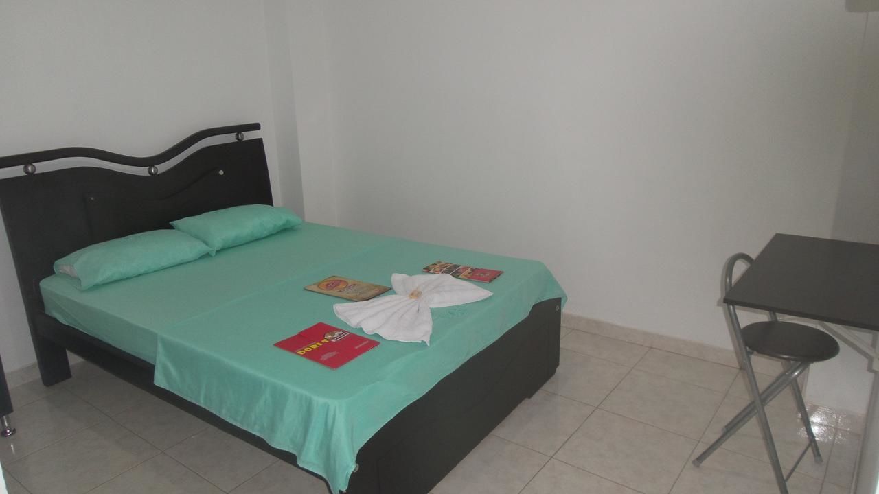 A single bed with a green bedspread, a white towel, and a red booklet on the bed.